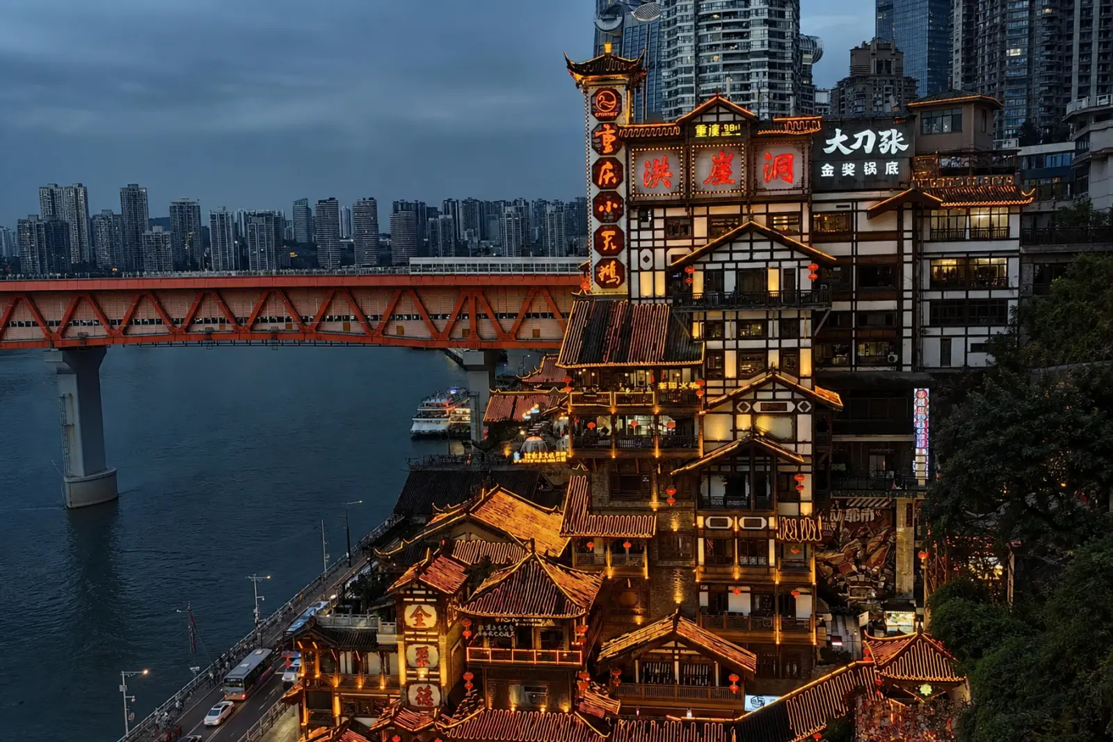 Hongya Cave illuminated at night beside the river and Qiansimen Bridge in Chongqing